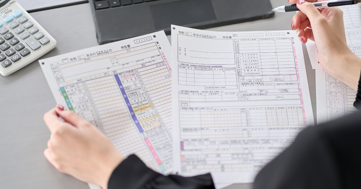 確定申告の書類を複数枚広げ、電卓を使って確認している人の手元