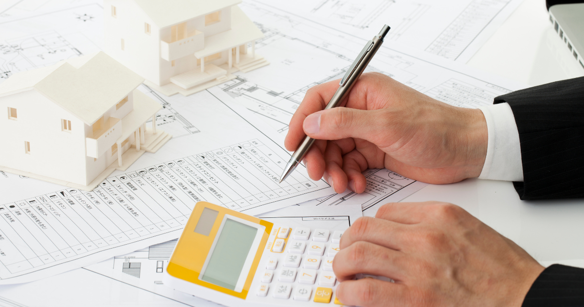 電卓と書類を机に置き、ペンを持って作業している男性の手元