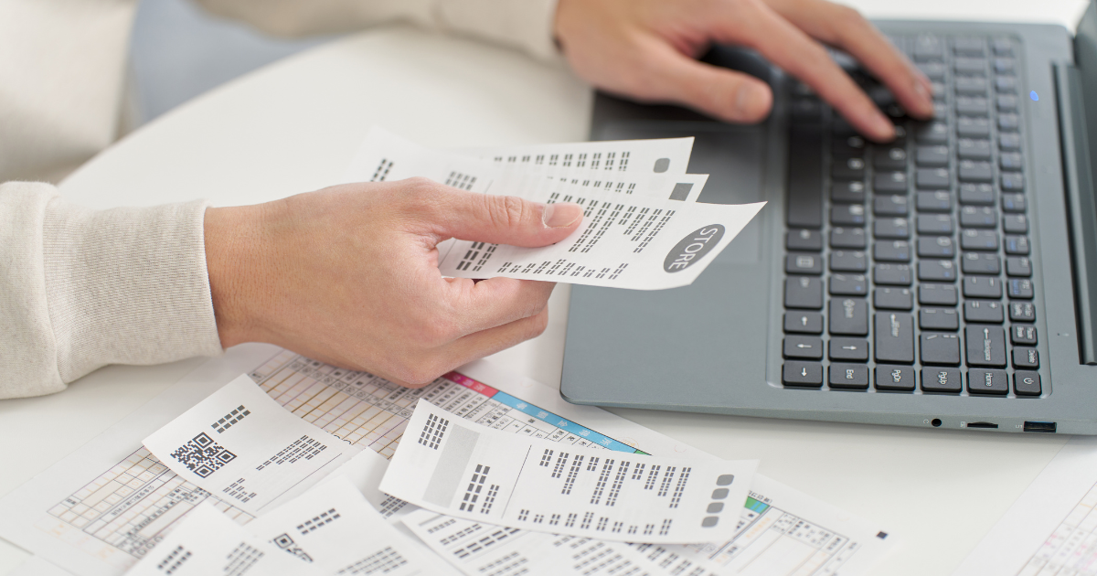 ノートパソコンのキーボード横でレシートを手に取って確認している男性の手元