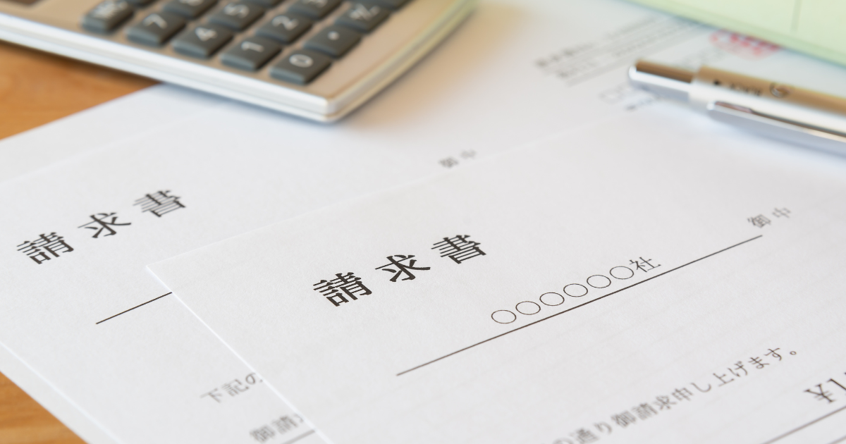 日本語で記載された請求書と電卓、ペンが机の上に並んでいる様子
