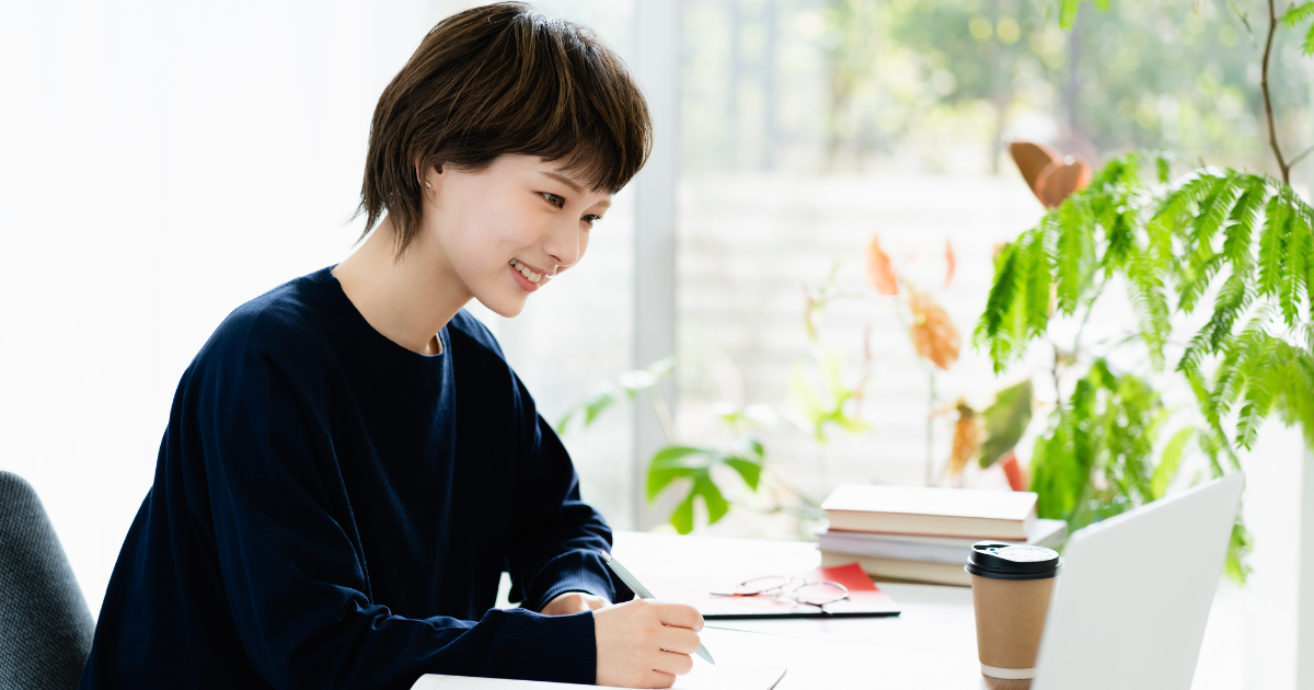 ノートパソコンを見ながら机で作業をしている女性