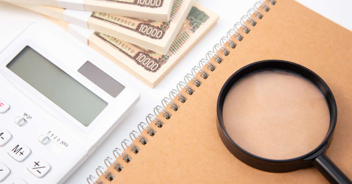 電卓と紙幣・ノートの上に虫眼鏡が置かれている