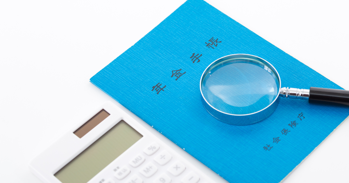 電卓の横の年金手帳の上に虫眼鏡が置かれている