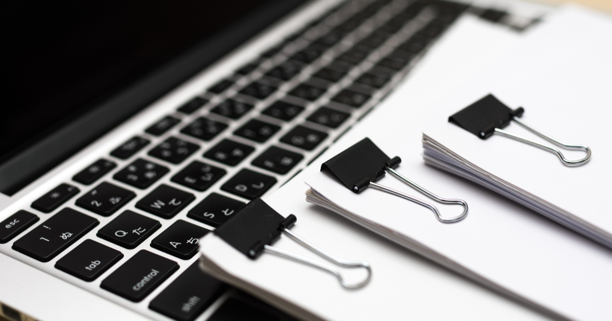 ノートパソコンのキーボードの上に、クリップで留められた書類が置かれている様子