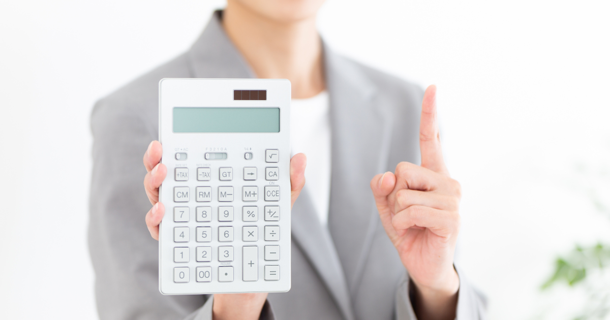 電卓を持ち、もう片方の手で人差し指を立てているスーツ姿の人物
