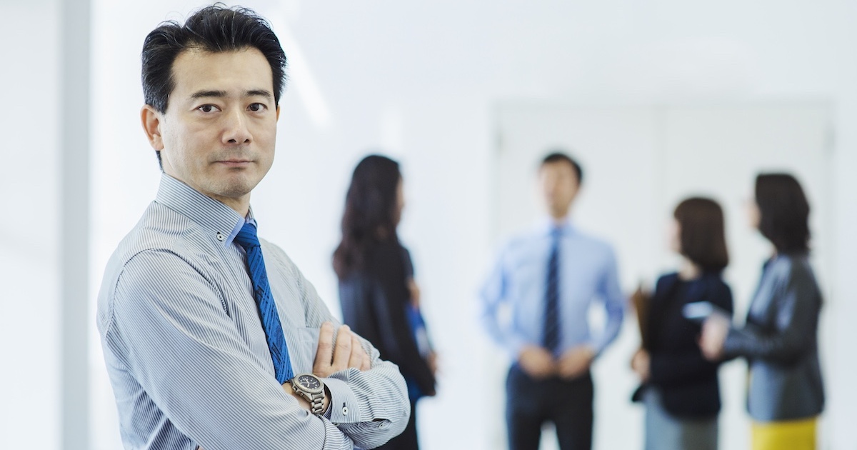 こちらを見つめるビジネスパーソンと背後に部下達