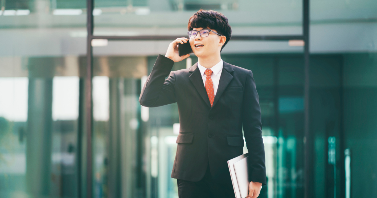 スーツ姿の人物が、建物前で電話をしながら歩いている