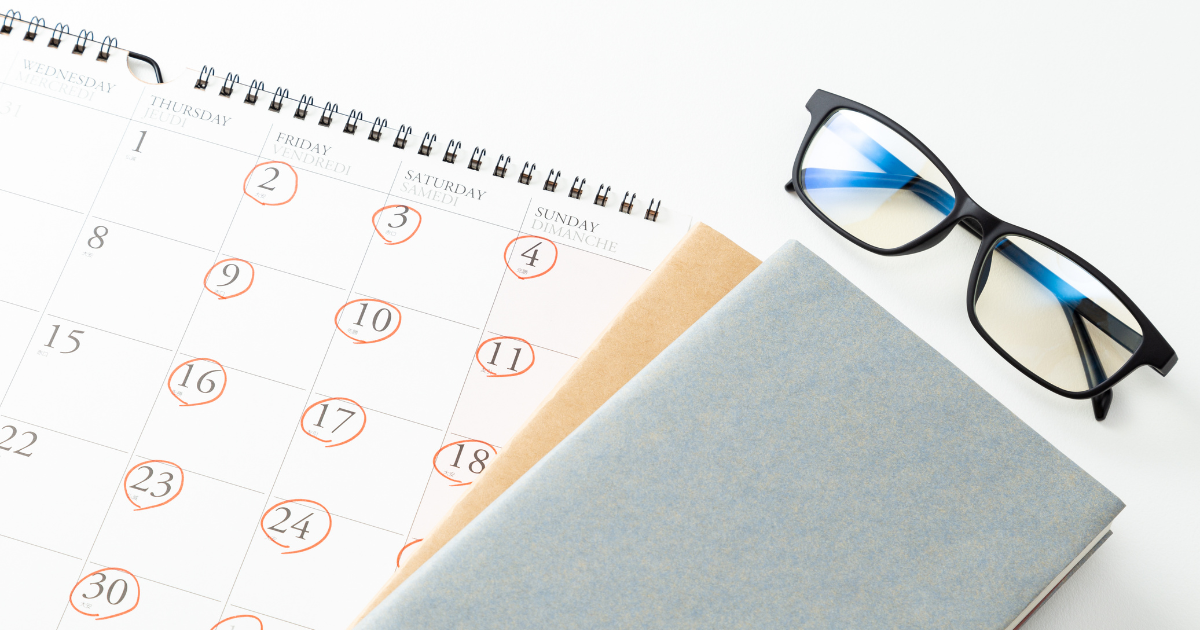 カレンダーの手帳とノート、眼鏡が机の上に置かれている