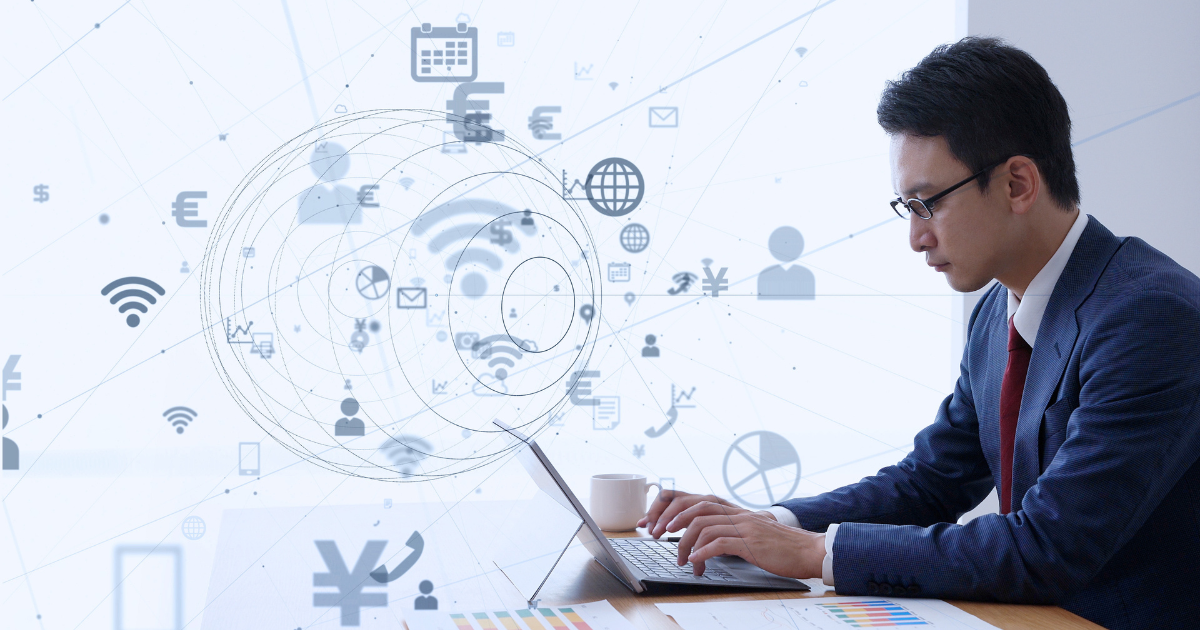 デジタル技術のイメージ図を背景にノートパソコンで作業するビジネスパーソン