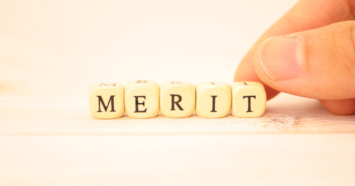 「MERIT」と書かれた木製ブロックを指で並べている手元
