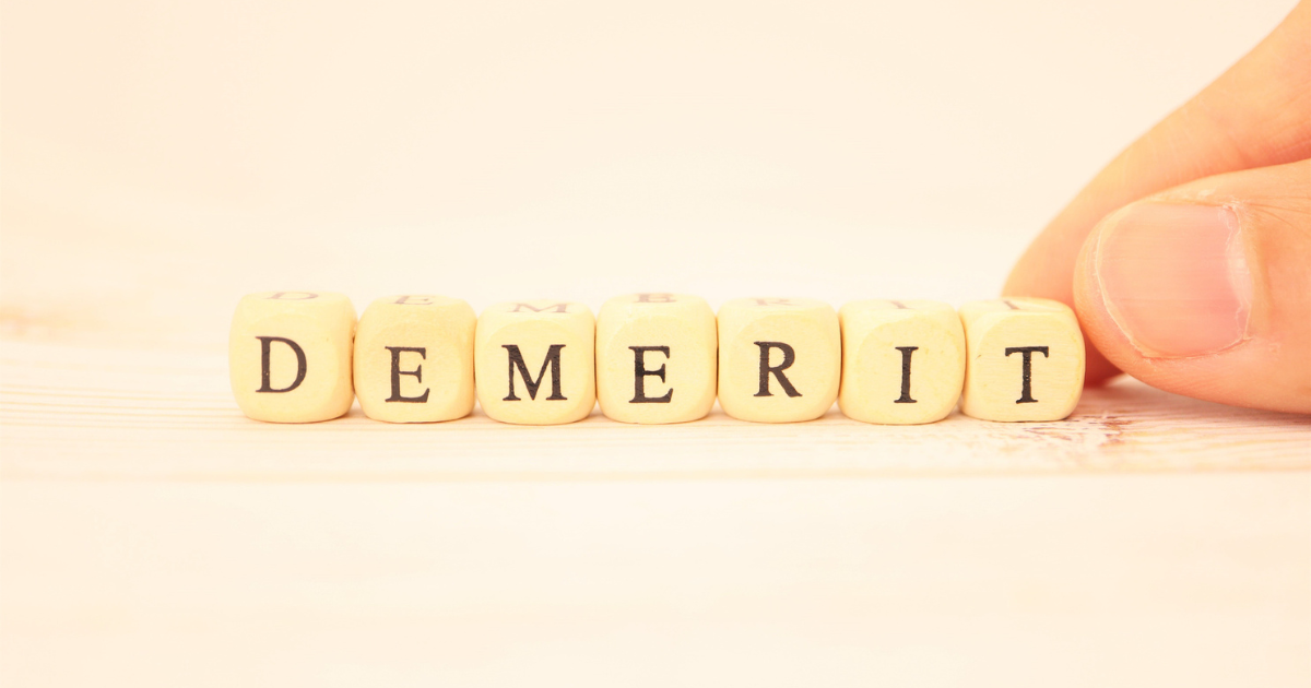 「DEMERIT」と書かれた木製ブロックを指で並べている手元