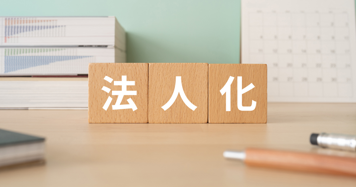 机の上に置かれた「法人化」と書かれた積み木と、書類や文房具