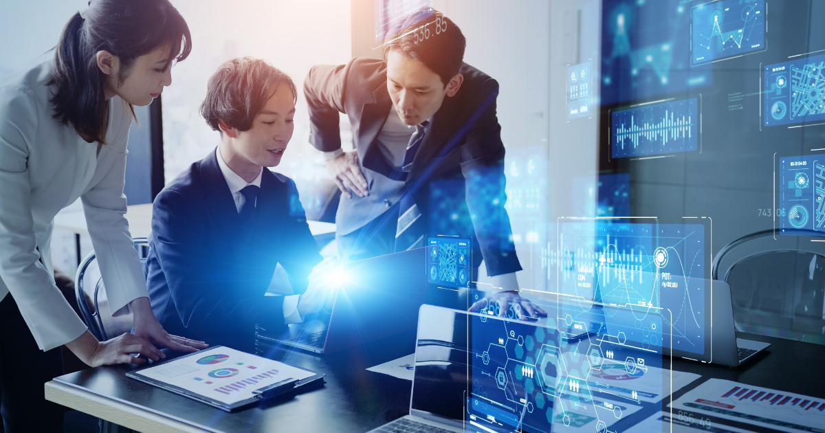 パソコン画面の光を囲みながら話し合うビジネスチーム