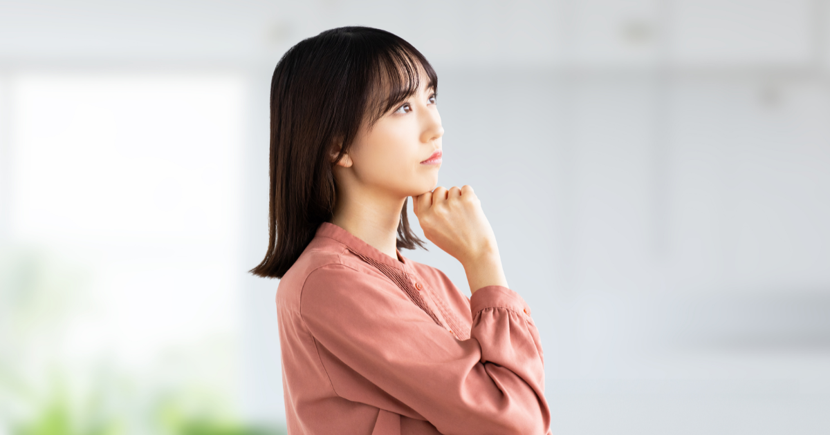 顎に手を当てて、遠くを見つめながら考え事をする女性