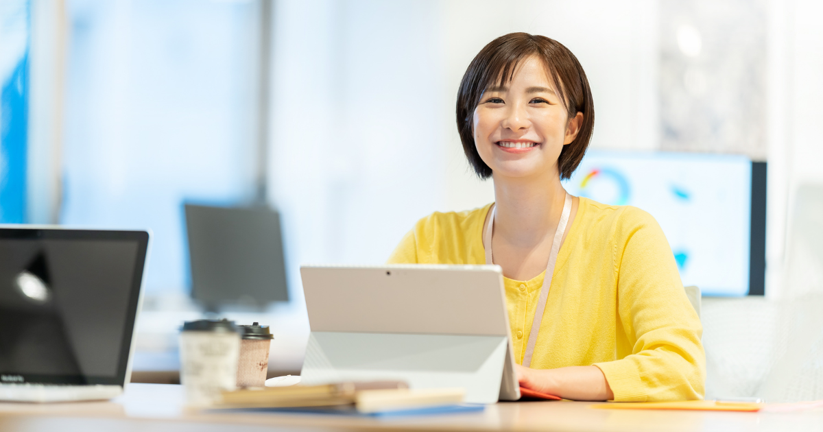 タブレットを開き、笑顔を見せる黄色い服の女性