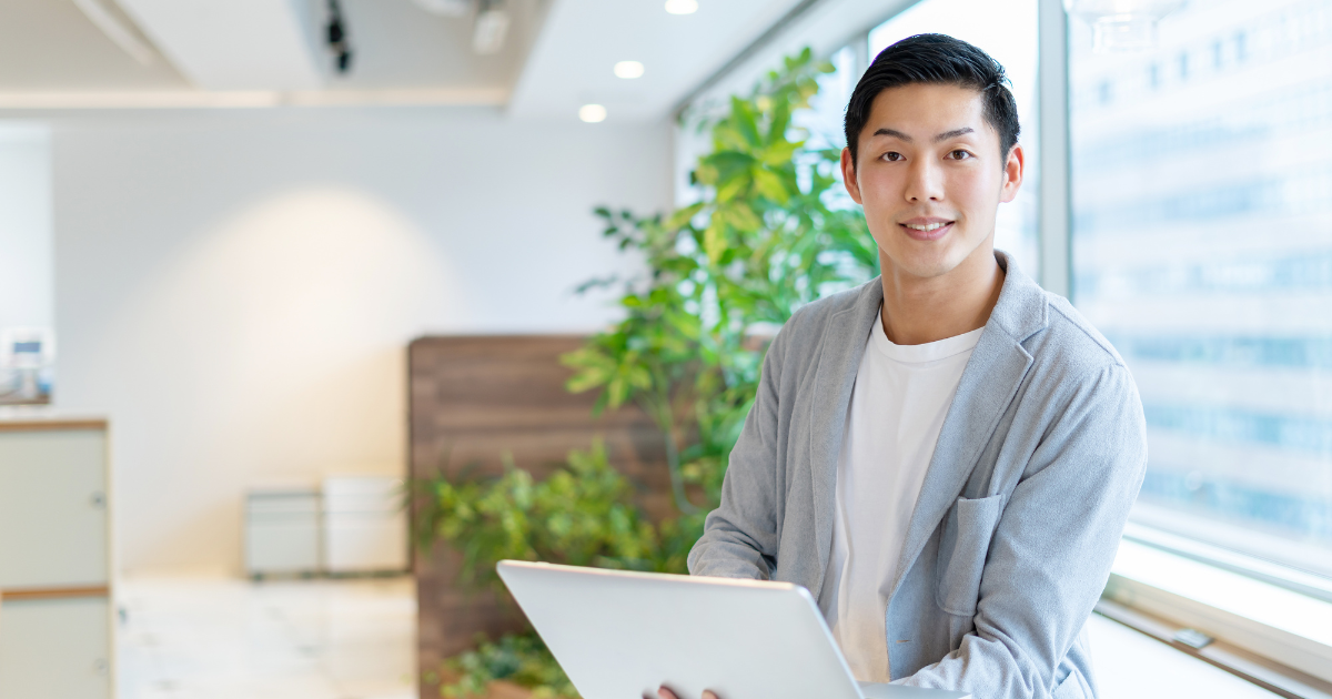 明るいオフィスでノートパソコンを持って立つ男性