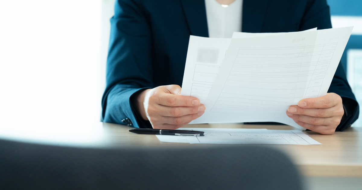 スーツ姿の人物が書類を手に持ち、内容を確認している