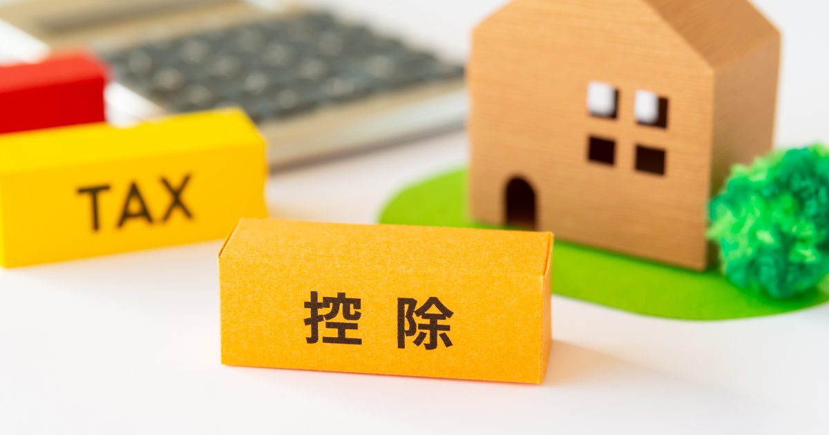 家の模型のそばに、「TAX」と「控除」と書かれたブロックが置かれている様子