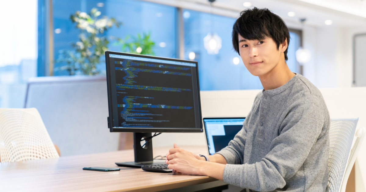 パソコンとモニターが置かれたデスクに座る男性