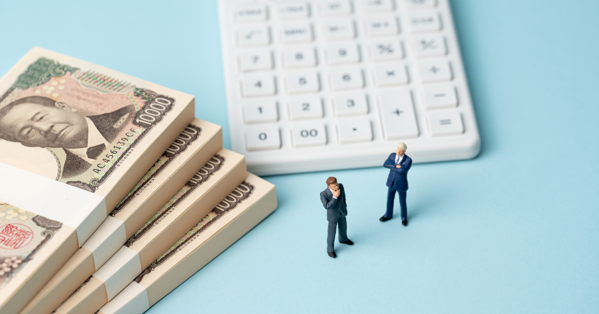積み上げられた札束と電卓、それを見つめるミニチュアのビジネスマン