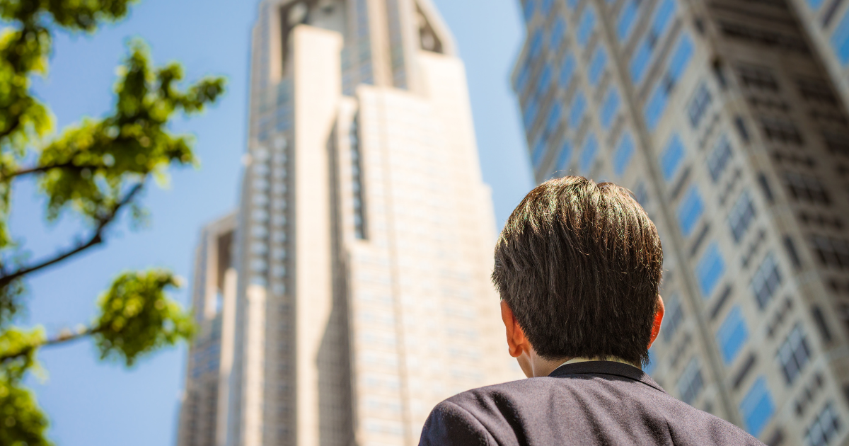 高層ビルを見上げるスーツ姿の男性の後ろ姿