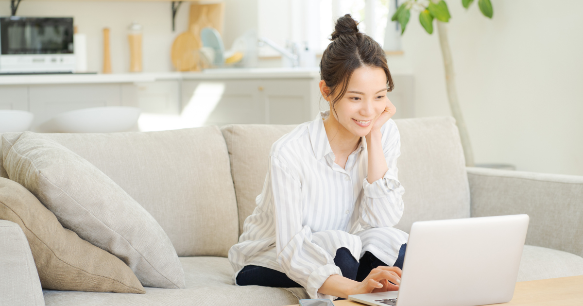 ソファに座ってリラックスしながらノートパソコンを使う女性