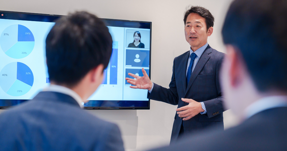 モニターのグラフを使ってプレゼンテーションを行う男性