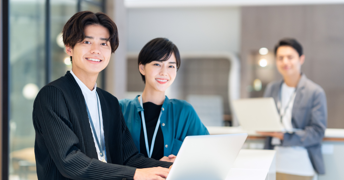 ノートパソコンを前に、カメラに向かって笑顔を見せる男女