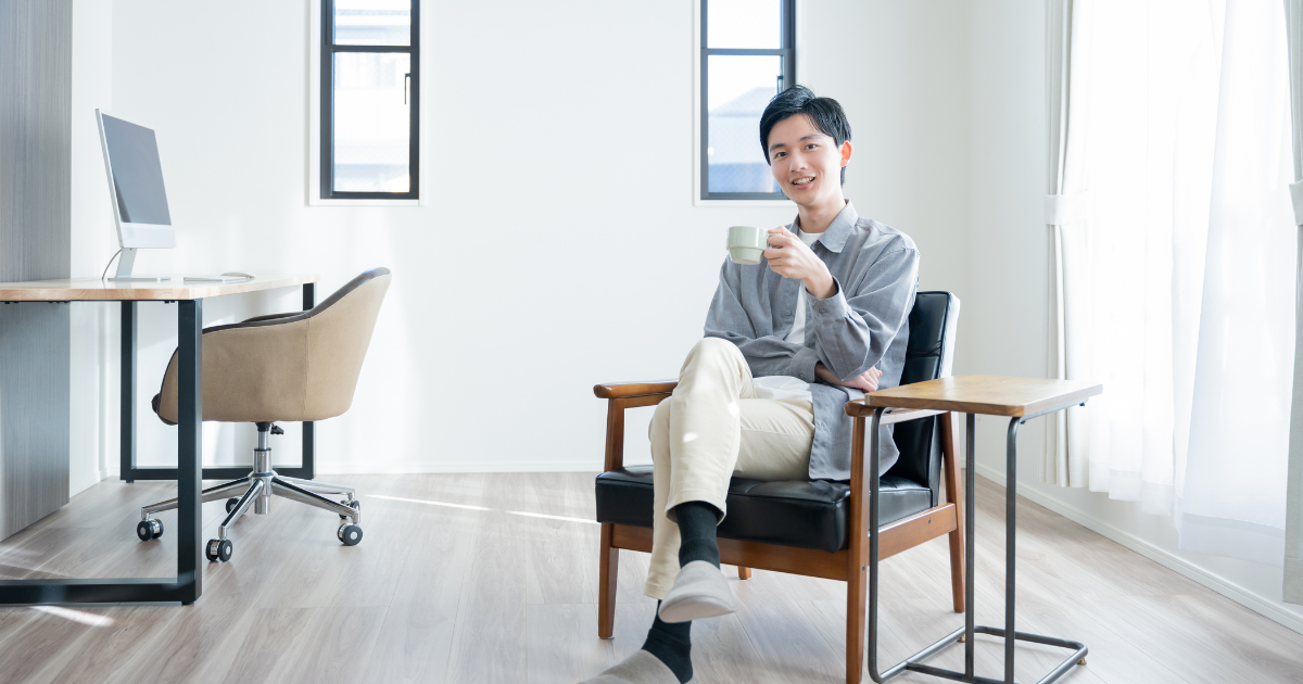 明るい室内で、椅子に座ってマグカップを持つ男性