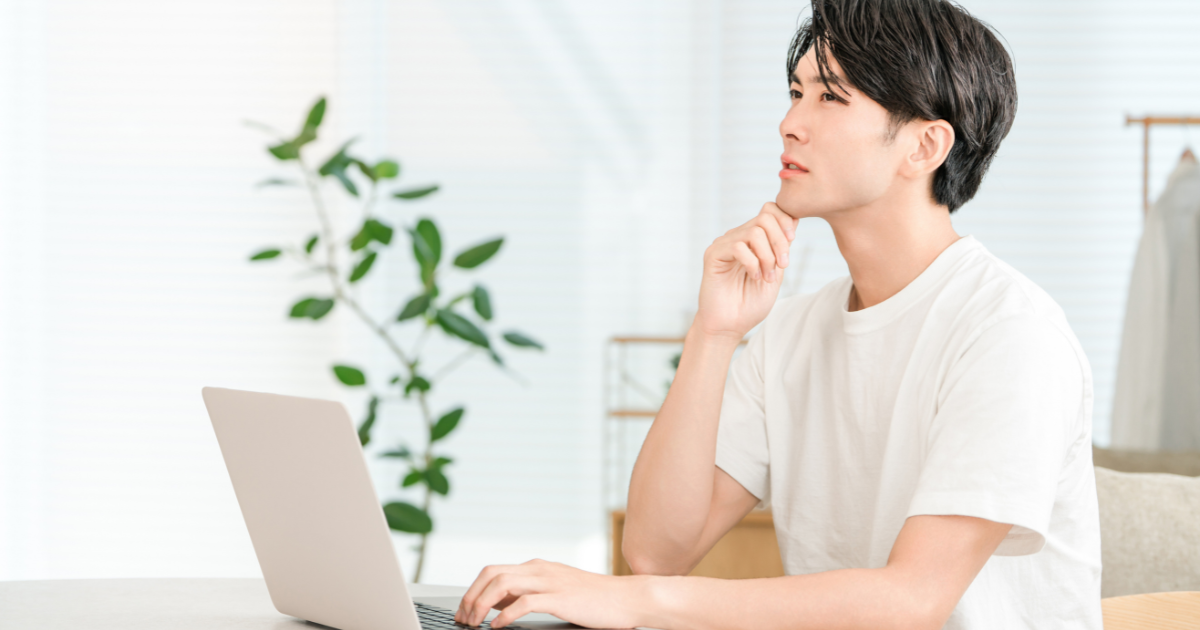 ノートパソコンの前で手を顎に当て、考え事をする男性