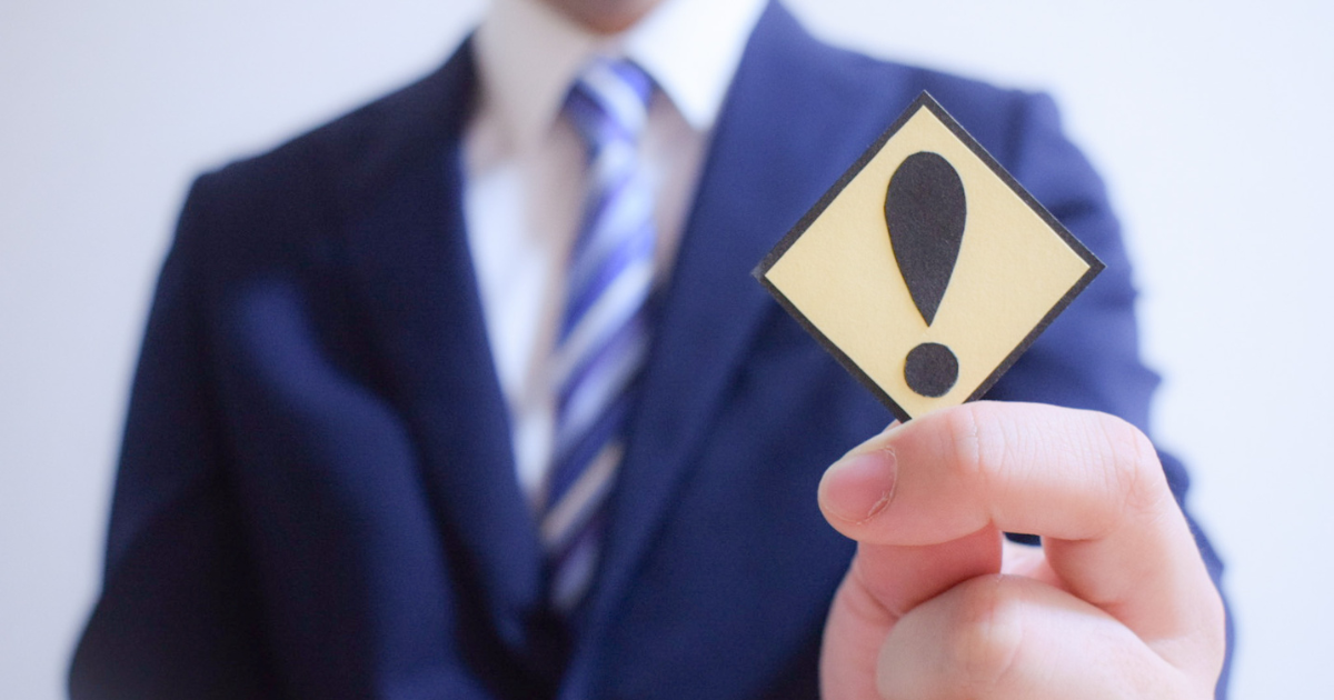 エクスクラメーションマーク（！）の札を持つスーツ姿の人物