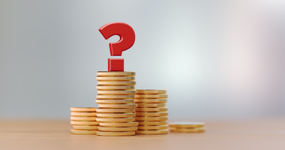 積み上げられた硬貨と、その上に置かれた赤いクエスチョンマーク