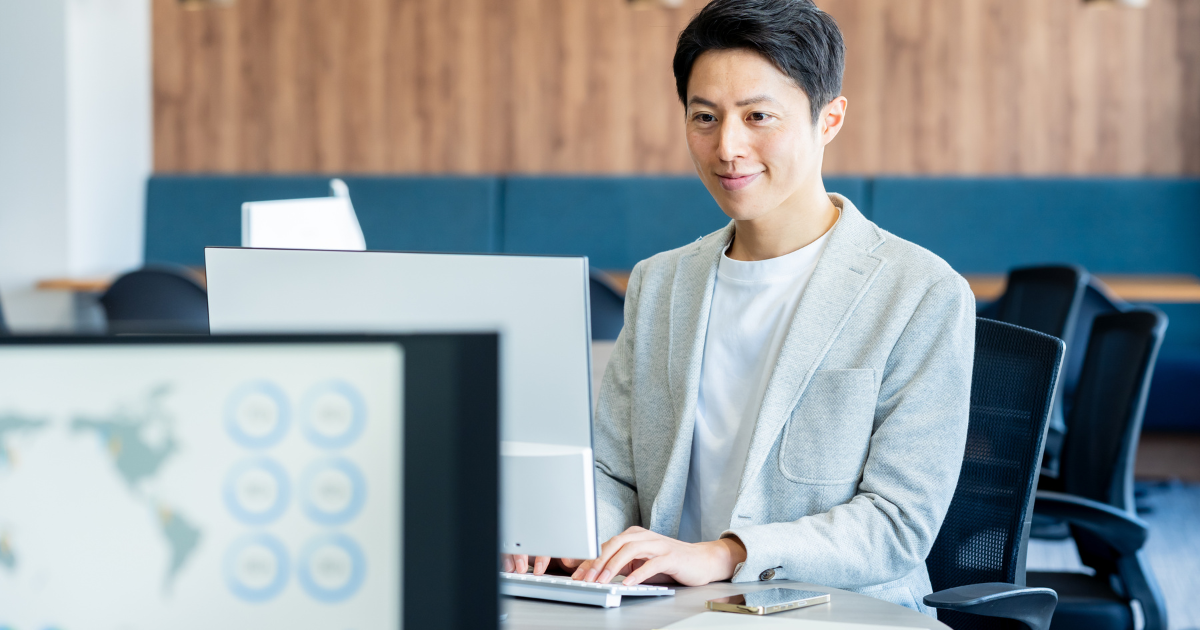 男性がオフィス環境で仕事をしつつ微笑んでいる