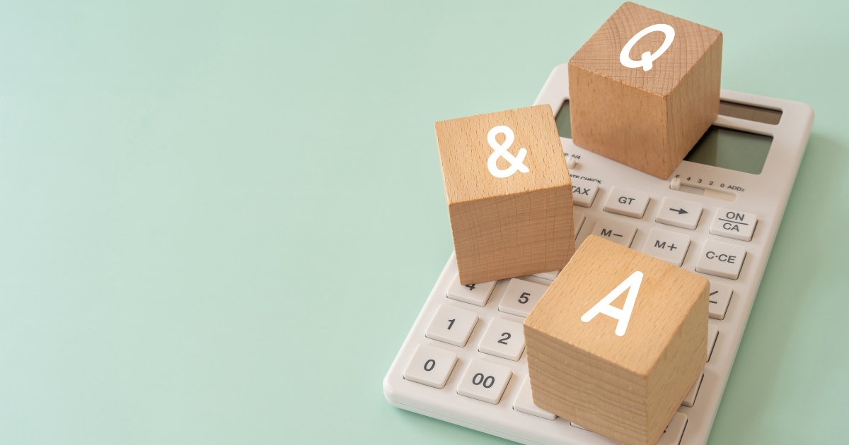 薄緑色の背景で、白い電卓の上に置かれた「Q」「&」「A」の文字が入った3つの木製キューブ