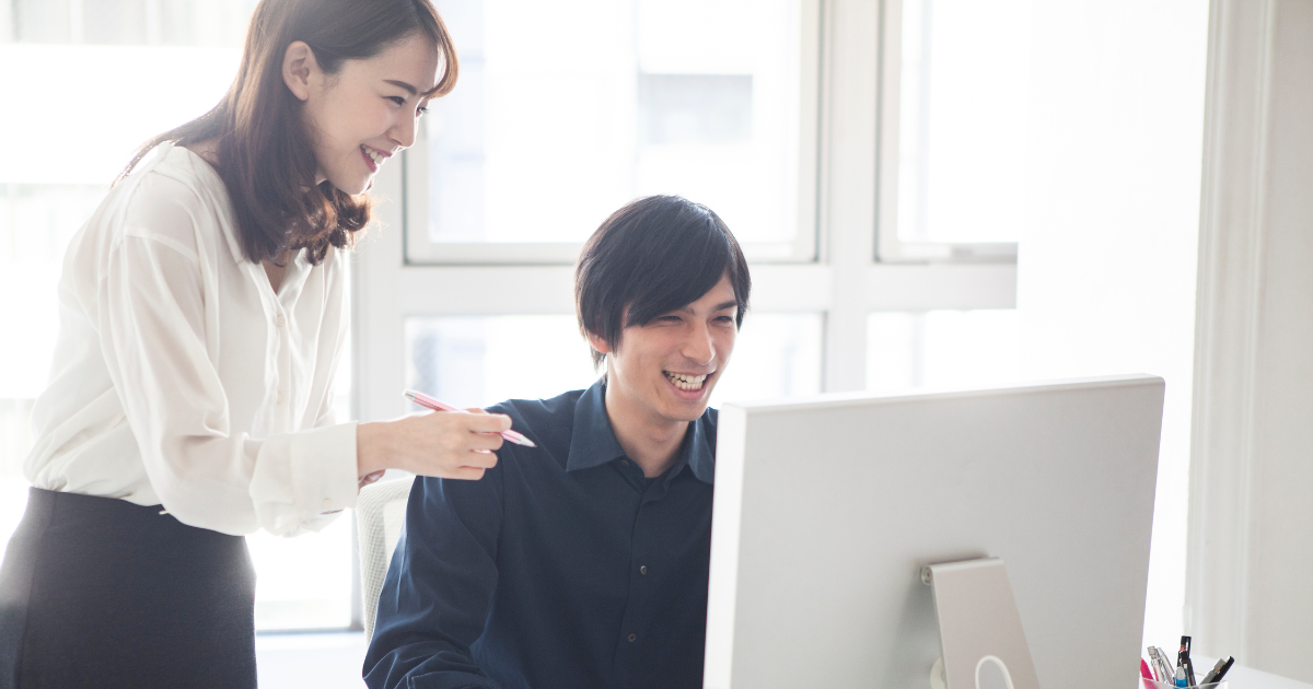 パソコンのモニターを見ながら笑顔で話す男女のビジネスパーソン
