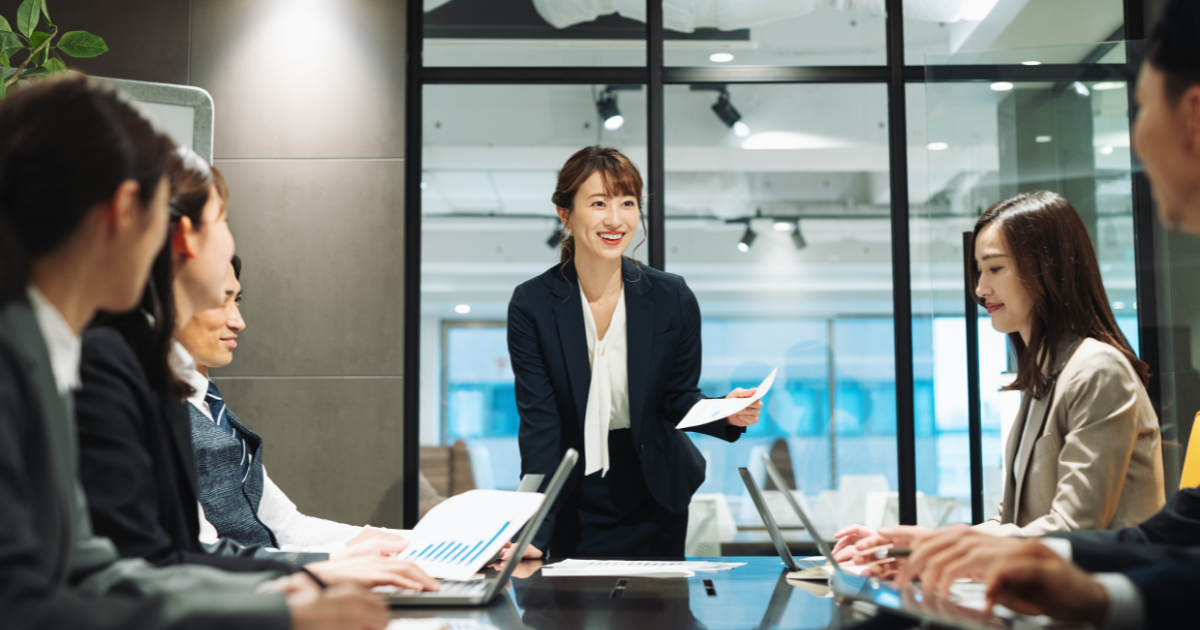 オフィスの会議室でテーブルを囲むメンバーに向かって話す女性