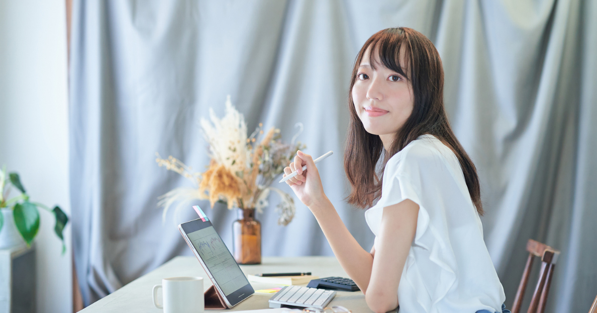 花が飾られた明るい室内で、タブレットを前にこちらを振り返る女性