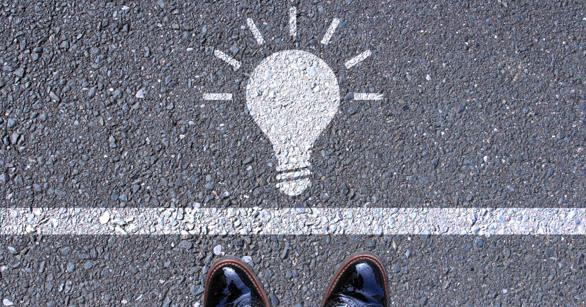 アスファルトに描かれた白線と電球のイラスト、手前に立つ人の足元