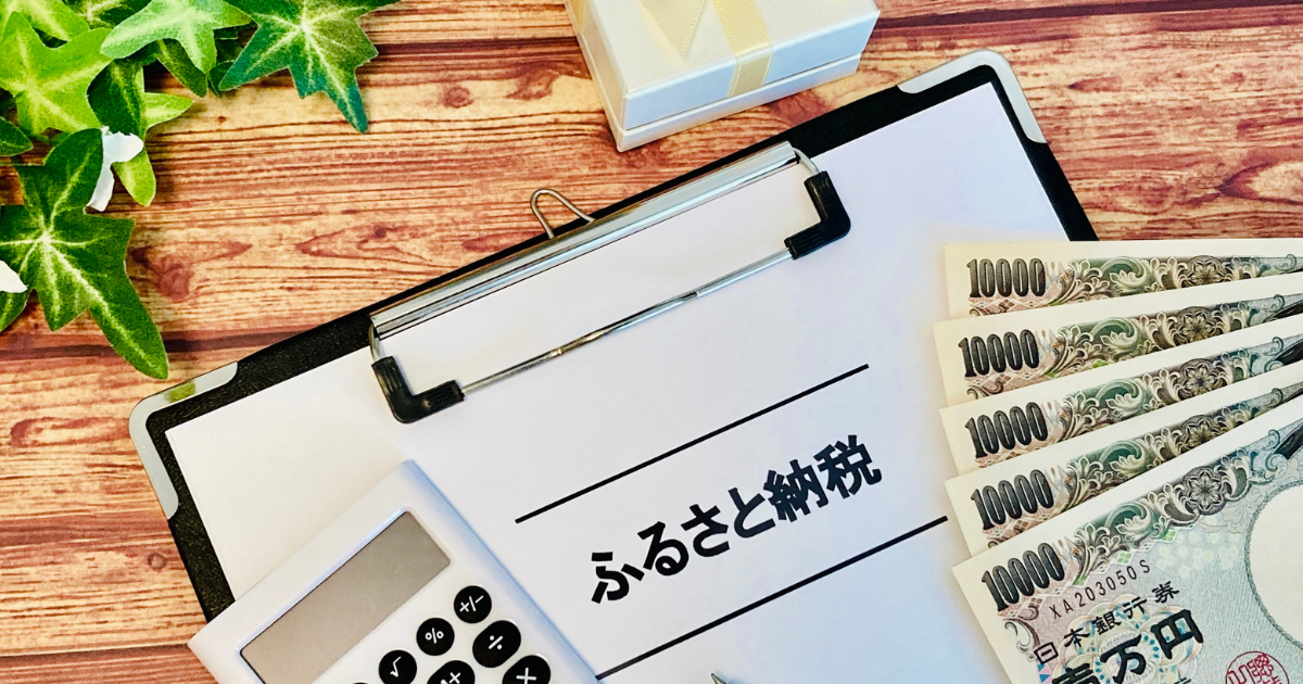 木製の机の上に置かれた「ふるさと納税」と書かれた書類、バインダー、電卓、複数の一万円札