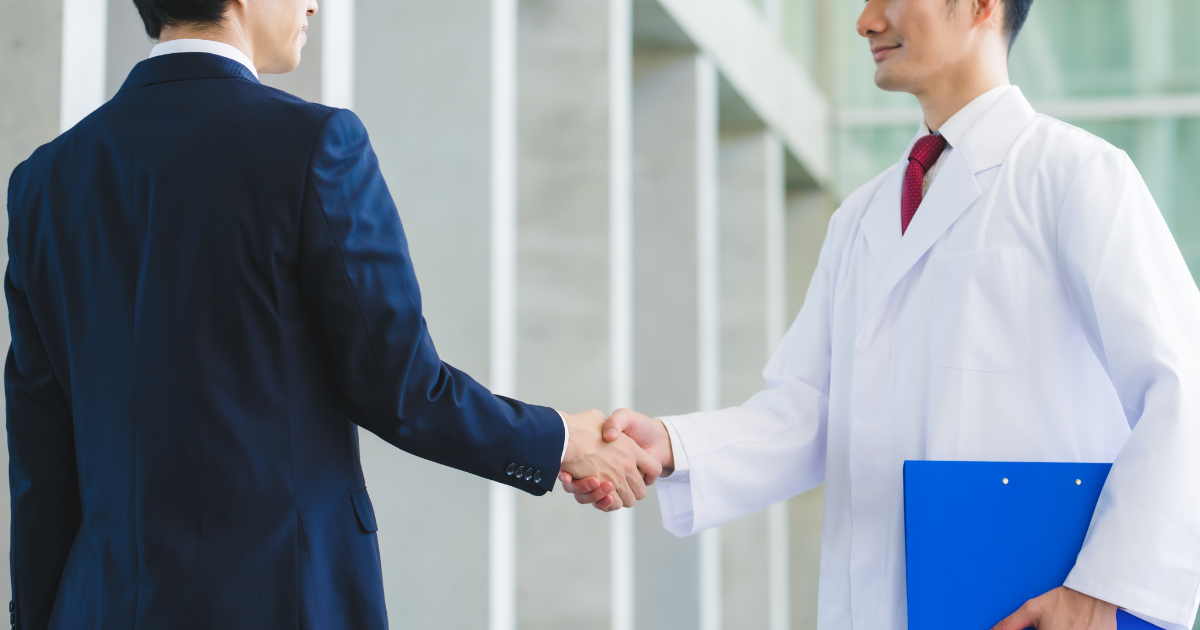 握手を交わすスーツ姿の男性と白衣を着た男性