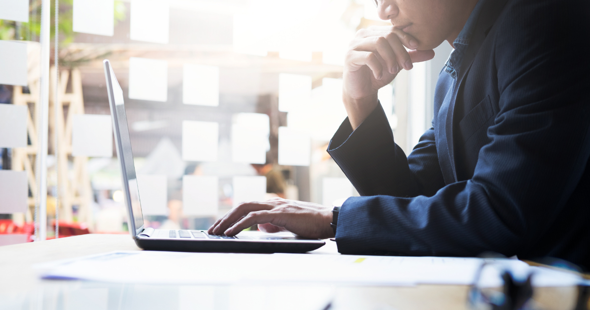 パソコンを開き、口元に手を当てて考え事をするスーツ姿の男性