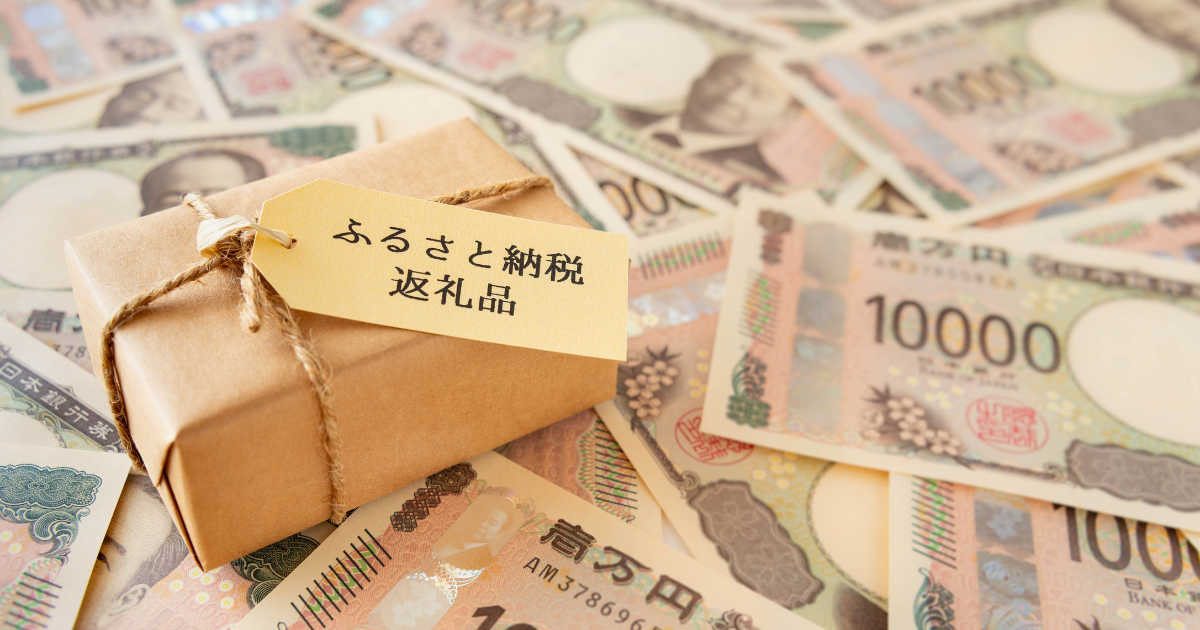 「ふるさと納税」と書かれたタグが付いたギフトボックスと、その周りに敷き詰められた多くの一万円札