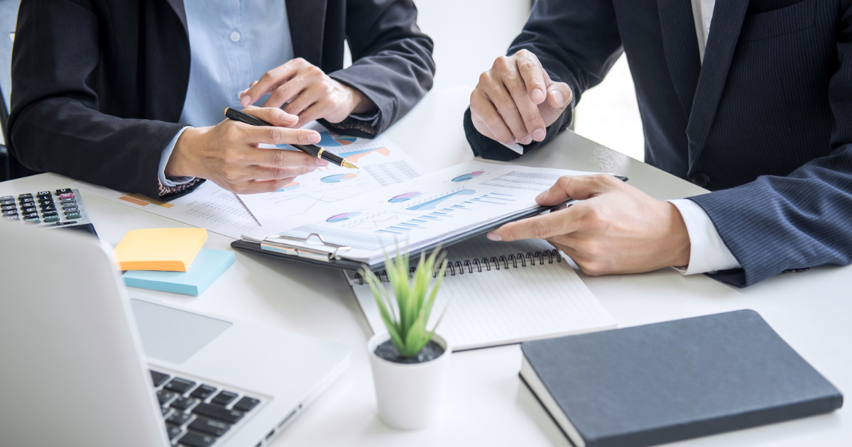 デスクで書類を見ながら打ち合わせをするスーツ姿の人々の手元