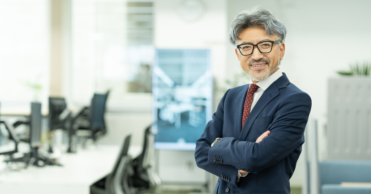 オフィスで腕を組んで微笑むベテランの男性ビジネスパーソン