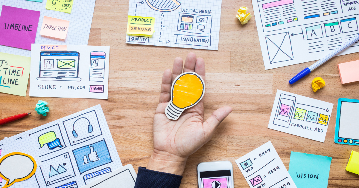 資料や付箋が広げられた机の上で、電球の形のカードを持つ手