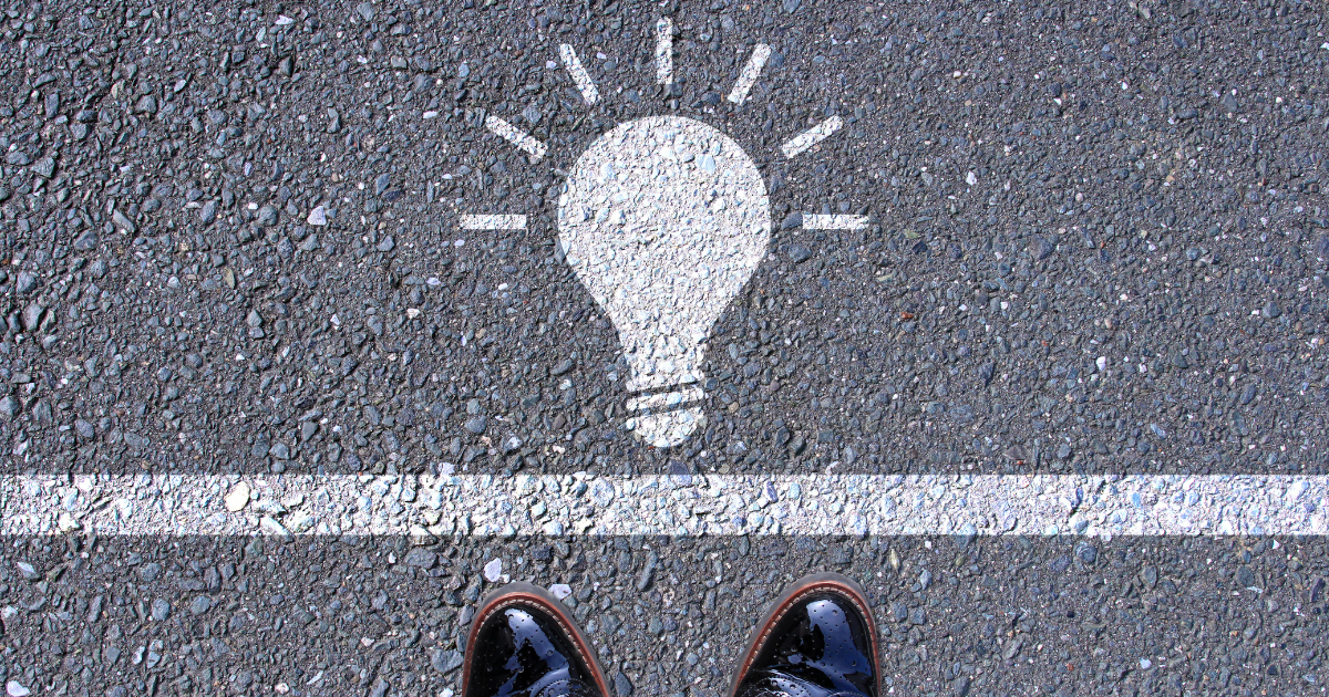 アスファルトに描かれた白線と電球のイラスト、その手前に立つ人の足元
