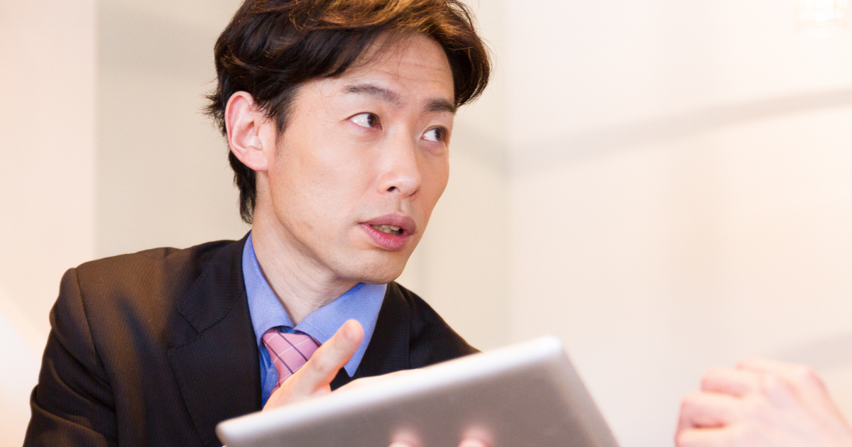 タブレットを手に持ち、相手に向かって説明しているスーツ姿の男性