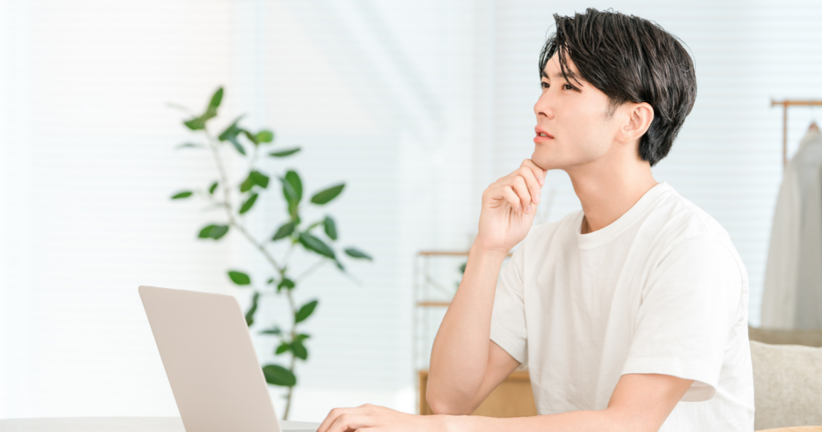 パソコンの前で頬杖をついて上を見上げながら考える男性