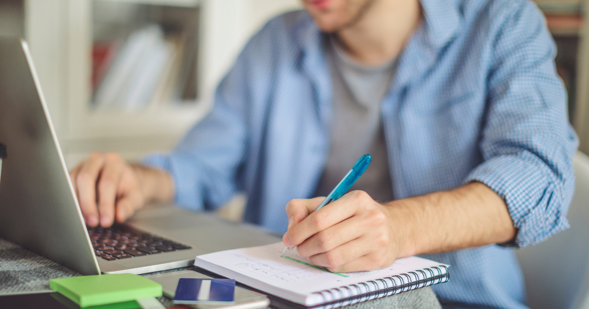 パソコンの前に座り、ノートにペンで書き込んでいる手元