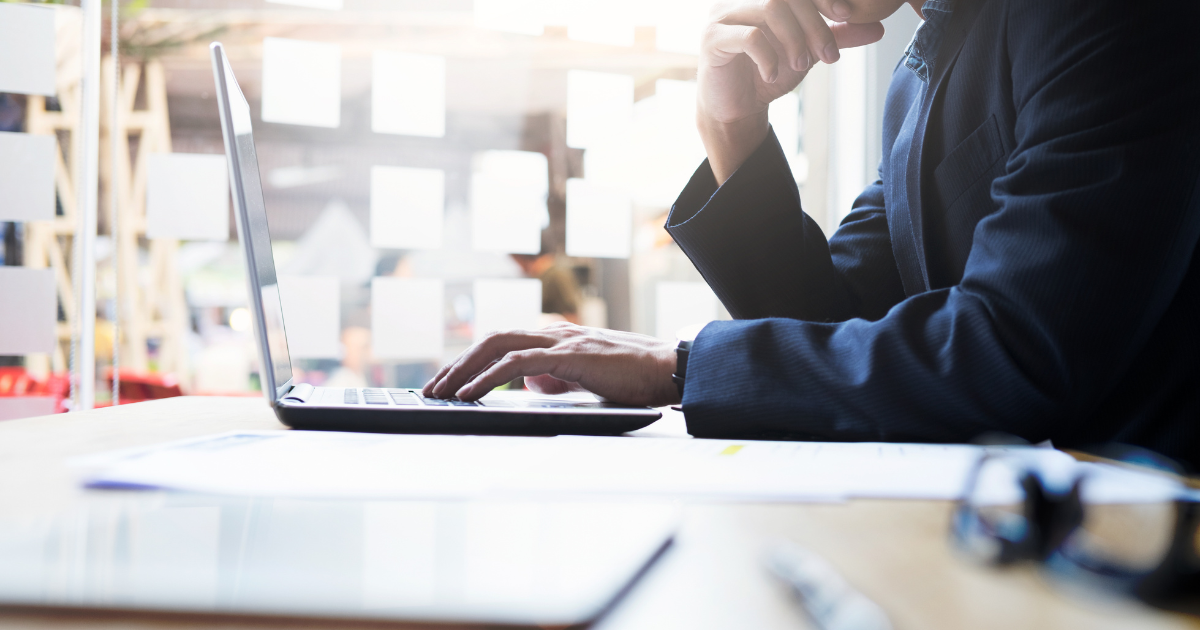 デスクでノートパソコンに向かい、考え込んでいるスーツ姿の男性